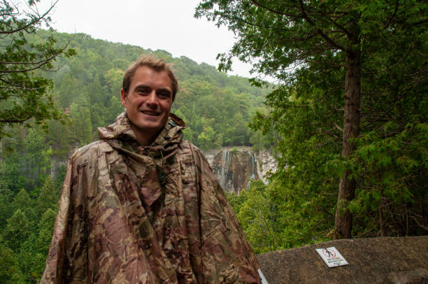 A man smiles at the camera in front of a waterfall