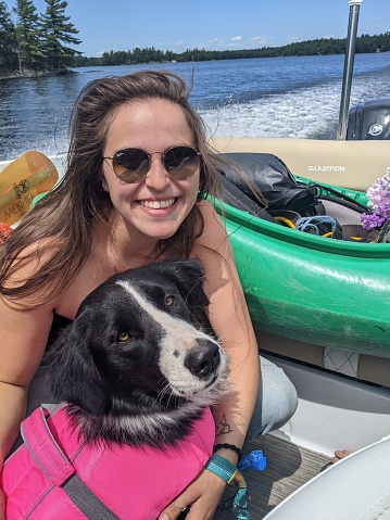 A woman holds her border collie dog on a boat moving over a lake