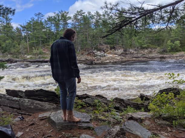 A woman stands beside a raging river