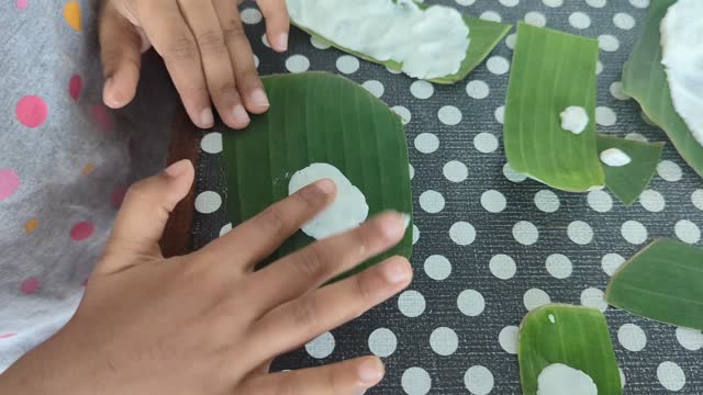 a person spreading food batter in a banana leaf with hand