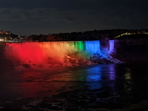 Niagara Falls is colorfully lit up at night with mist coming off the water