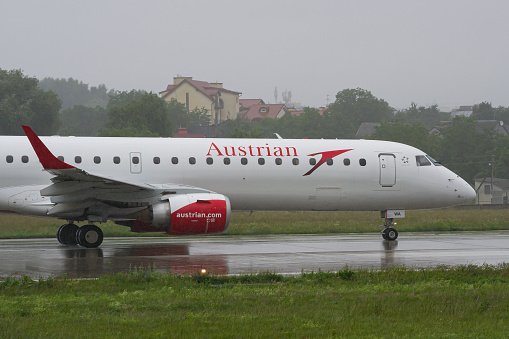 Close-up of an Austrian Airlines Embraer E195 aircraft taxiing during rain to the runway for takeoff from Lviv Airport