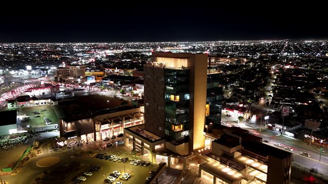 Drone hyperlapse of illuminated city with Metrocentro commercial zone building at night