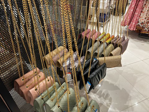 A display of purses with gold chains hanging from the ceiling. The purses are of different colors and styles