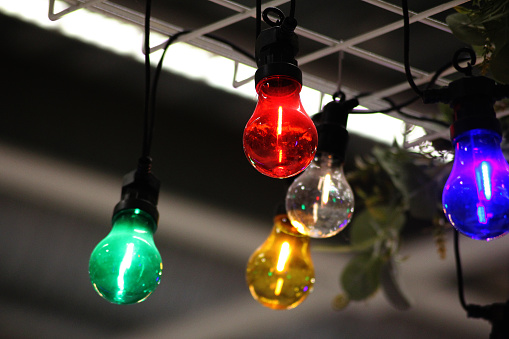A green , red , yellow, white and purple light bulb hanging from the ceiling