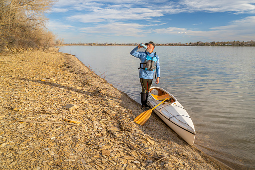 Self portrait of a senior male paddler with expedition decked canoe on a lake shore in early spring, Boedecker Reservoir in northern Colorado