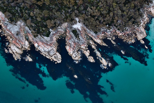 A Top-down aerial colourful rocks with clear blue ocean Bay of fires Saint Helens, Tasmainia