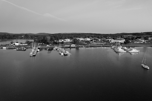 A black and white photo of a peaceful harbour with a sail boat in the water