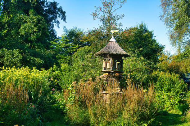Large structure made of wood and thatch in a mature garden, with nesting boxes for birds and an insect hotel