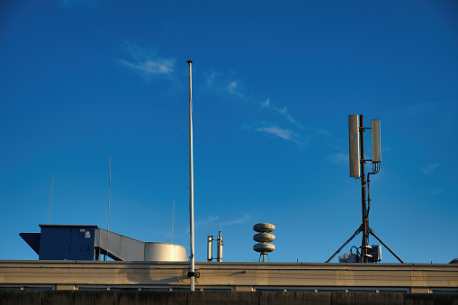 Structures on the roof of a building, a.o. an air raid siren and telecommunication network antenna panels, under a blue sky. The Hague, the Netherlands