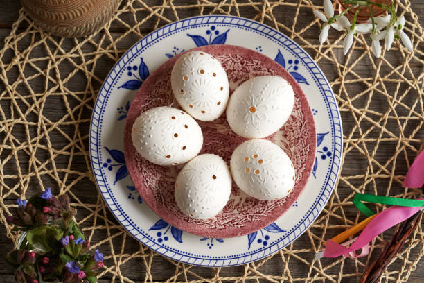 istock White Easter egg decorated with wax and drilled holes, with spring flowers - snowdrops and lungwort 2144104603