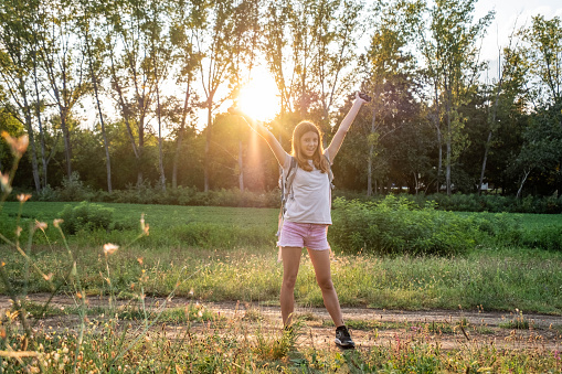 portrait of happy teenage girl in nature on meadow with open arms smiling, sorc, sun, hiking backpack