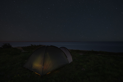 Camping with a tent in nature by the sea at night under the starry sky in Estonia. Low light photo