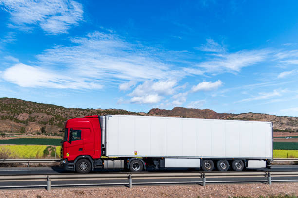 istock Truck with refrigerated semi-trailer driving on a road between vegetable fields, side view. 2144175794