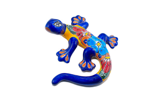 Mexican ceramic pottery of a salamander, gecko or lizard indoor outdoor wall art painted multi colored blue, red, yellow, orange with flower pattern design, isolated on white background