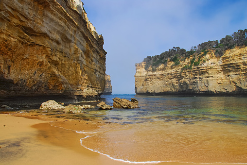 Dramatic cliffs guard the entrance to a small ocean bay and beach on the southern coast of Victoria, Australia.