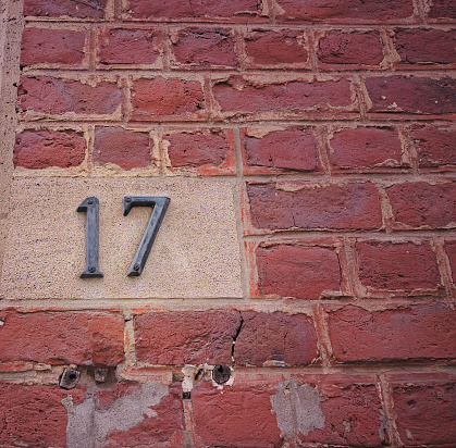 Number with the number seventeen or 17 in Latin. An old red brick wall with signs of destruction. Covered with cracks. Non-uniform surface texture.