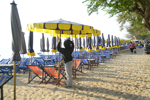 Phetchaburi , Thailand - January  9 , 2024 : An unidentified Asian male was setting up umbrellas and beach chairs for the day's tourists on January 9 ,2024 at Cha Am beach in Phetchaburi Province ,Thailand.