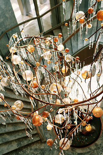 Long branching chandelier with pendants and balls hangs between floors in a hotel. High quality photo