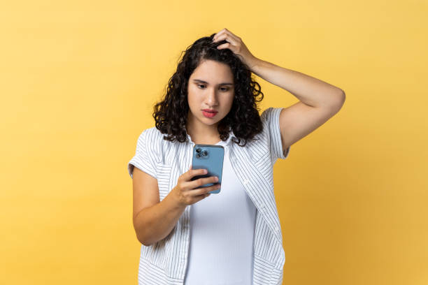 istock Pensive beautiful woman using cell phone thinking what to answer, keeps hand on head. 2144527741