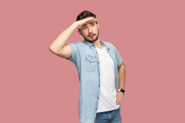 istock Man with palm near forehead, looks with concentrated expression into distance, sees something aside. 2144529418