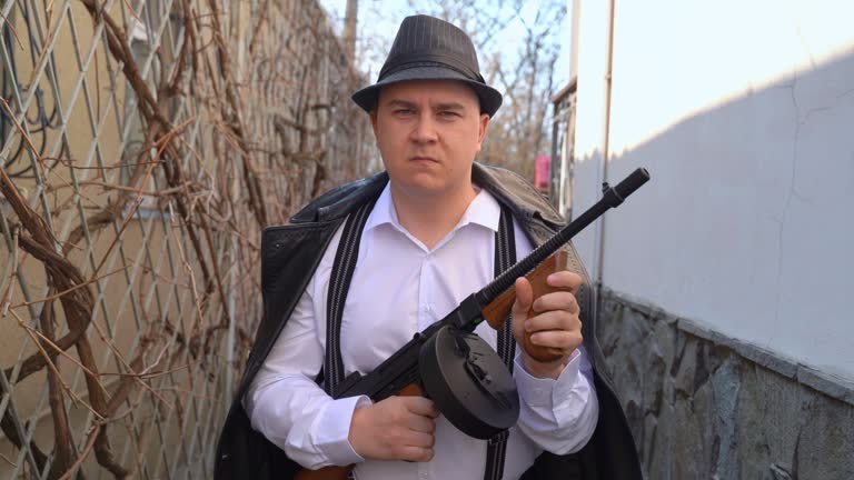 Man in a fedora and jacket holding a shotgun with a serious expression outdoors, implying a concept of defense or vigilance