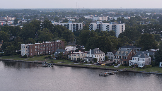 Elizabeth River bank and residential houses on foreground. Wealthy townhouses and parking lots on the Swimming Point riverside. Downtown Portsmouth, VA in the distant. Aerial view
