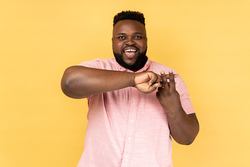 Portrait of popular man blogger wearing pink shirt making hashtag sign with fingers, looking at camera with smile, tagging posts in social networks. Indoor studio shot isolated on yellow background.