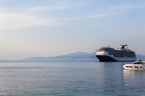 Kusadasi bay, cruise ship sails past on tranquil waters of Aegean see against of soft-hued mountains at dusk as background. Aydin province, Turkiye (Turkey). October 22, 2023