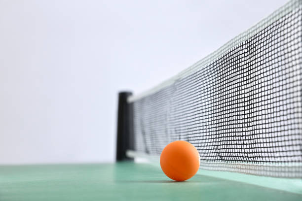 Ping pong background with orange ball next to the net on a green game table and white isolated background. Front view.