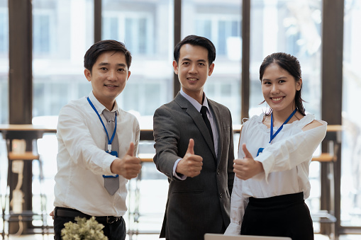 Successful young asian business people with thumbs up. looking at camera.