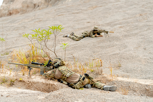 Two military or soldiers lie down on the ground with hold gun point to the opposite side on battlefield or outdoor practice area.