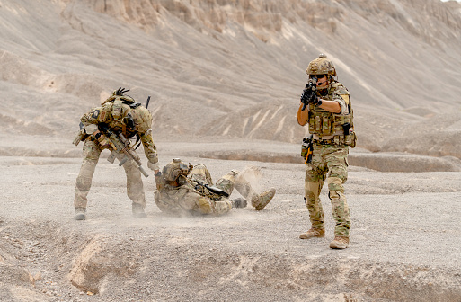 One of military or soldier try to pull member of his team along the way to escape the danger and protect by the other one point gun to front in area of practice or outdoor battlefield.