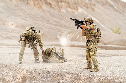 One of Military or soldier try to pull member of his team along the way to escape the danger and protect by the other one point gun to front upper to enemy in area of practice or outdoor battlefield.