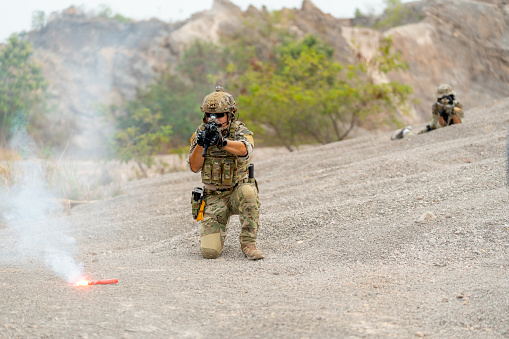 Two military or soldiers with hold gun and stay in different area to practice fighting in battlefield with one flare on the ground in front of them.