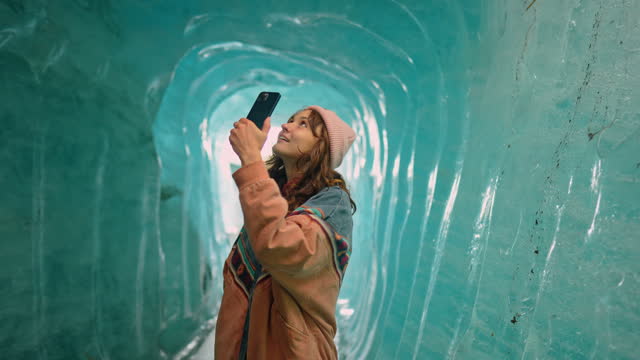 Woman photographing with smartphone in ice cave