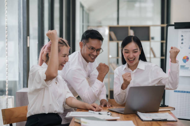 Enthusiastic Asian business team celebrating a successful project in office. Group achievement and teamwork concept.