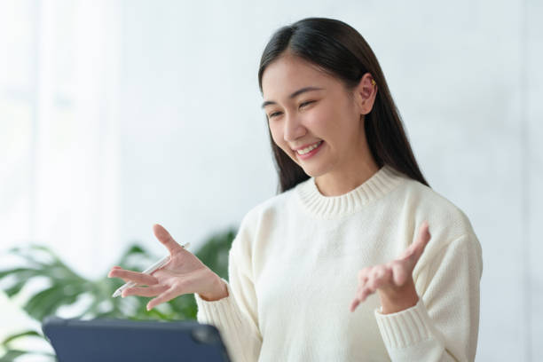 istock Beautiful young Asian woman college student is video chatting with her classmates using laptop, smiling faces and gestures happily studying. 2144967621