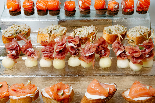 An array of gourmet canapés featuring smoked salmon on bread and prosciutto with melon balls, beautifully presented for a catered event.