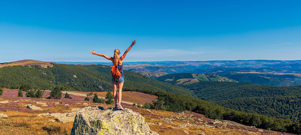Happy girl with arms raised up standing on mountain peak enjoying panorama landscape view- Travel, freedom,achievement,adventure concept