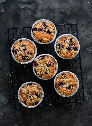Blackcurrant muffins with crumble on a baking rack on a dark background, top view