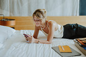 Portrait of a Beautiful Smiling Modern Woman Lying on the Bed in a Hotel Room and Texting on Her Phone