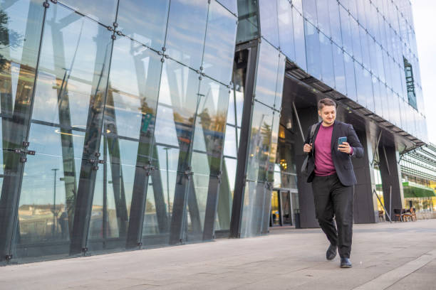 istock Young businessman typing text message on his way to work while walking near the urban corporate building. 2145252242