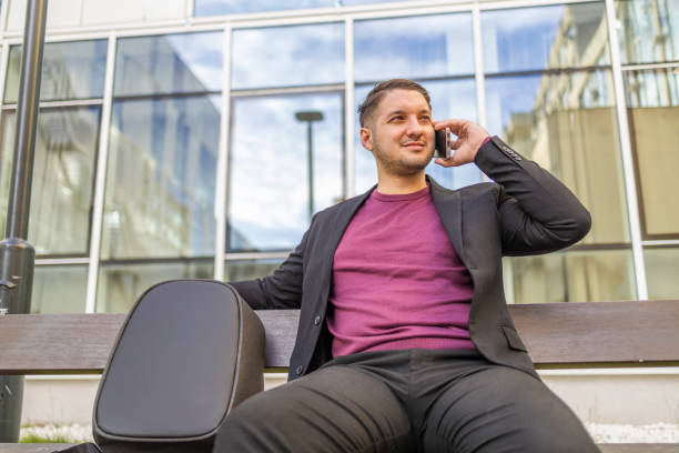 istock Young businessman  using mobile phone while sitting on the bench near the office. Business concept 2145255992