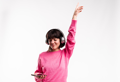 Studio portrait with white background of a young woman dancing raising arm listening to music with mobile