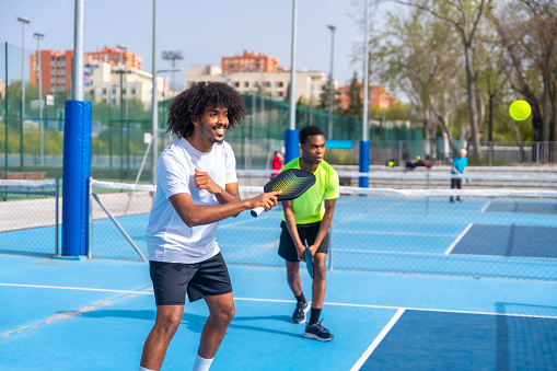 Two african american young sportive male friends enjoying playing pickleball together in an outdoor court