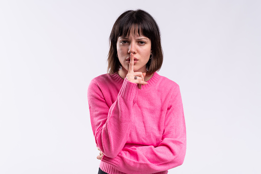 Studio portrait with white background of a woman asking for silence finger on mouth