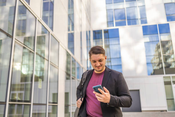 istock Young businessman typing text message on his way to work while walking near the urban corporate building. 2145258135