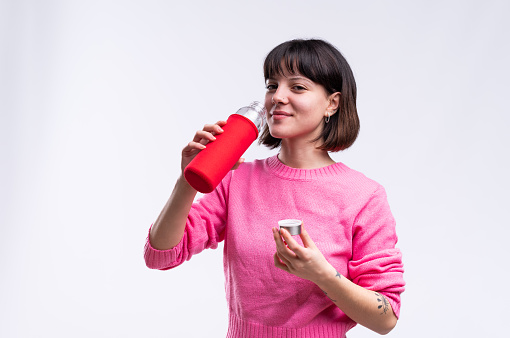 Studio portrait with white background of a young woman drinking water from reusable bottle