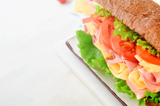 Sandwich. One fresh big submarine sandwich with ham, cheese, lettuce, tomatoes and microgreens on light background. Healthy breakfast theme concept, school lunch, breakfast or snack.
